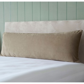 Belledorm Velvet Bolster Cushion in taupe, long rectangular shape, styled on a bed with white bedding against a sage green panelled wall.