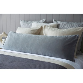 Belledorm Velvet Bolster Cushion in Cloud grey, styled on a bed with cream and textured cushions against a panelled headboard.