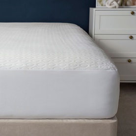 Belledorm Cooling Memory Foam Mattress Protector in white, fitted to a double bed with quilted texture, beside a bedside table.