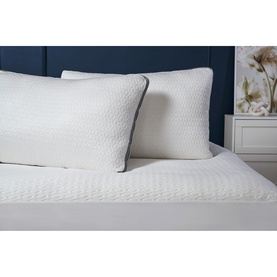 Belledorm Cooling Memory Foam Mattress Protector in white on a bed, styled with two white quilted pillows against a navy headboard.