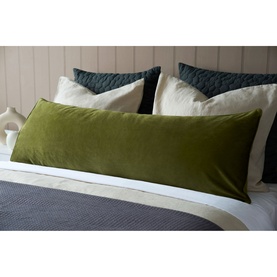 Belledorm Velvet Bolster Cushion in olive green, styled on a bed with cream and teal pillows against a neutral headboard.