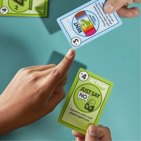 Hands holding green and white game cards on teal surface, showing Action and Role card gameplay from a multi-card game set
