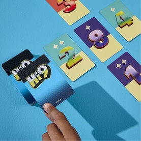 Hand holding a multicoloured numbered card from a Board Games card game, with additional number cards spread on a blue surface.