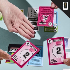Board Games Monopoly FIFA World Cup edition showing pink and multi-coloured playing cards with number 2 and transfer cards being held by hands.