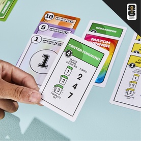 Board Games Monopoly card game, multi-coloured player cards including Center Forward and Match Winner spread on a light blue surface, hand holding