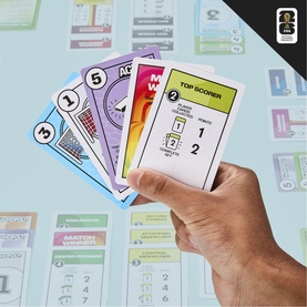 Hand holding Monopoly Access edition cards in multi-colour, showing Top Scorer and numbered game cards, with game board visible below.