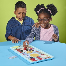 Two children playing Monopoly board game at a blue table, one reaching excitedly to move a piece, colourful multi-themed board visible