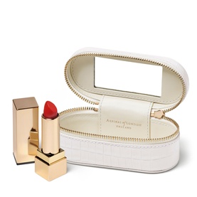 Aspinal of London Chalk White croc-effect oval travel jewellery box with mirror lid, gold zip trim, styled with red lipstick.