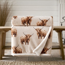 Deyongs beige Highland cow print throw with sherpa reverse, draped over a wooden bench in a neutral home setting