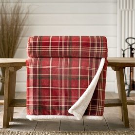 Deyongs red tartan throw with sherpa fleece reverse, draped over a rustic wooden bench in a cosy home setting