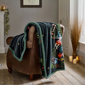Deyongs navy festive throw draped over a brown armchair, featuring Christmas nutcracker print with green sherpa trim, styled in a cosy living room