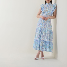 Model wearing Elliatt blue multi floral tiered midi dress with ruffle trim, lace inserts, and sleeveless design, styled with white heeled mules