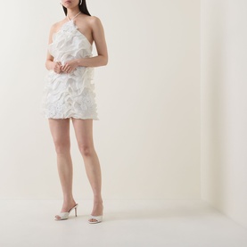Model wearing Elliatt white mini dress with feather-trim detail and one-shoulder neckline, styled with strappy heeled mules