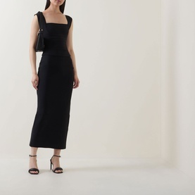 Model wearing Elliatt black midi skirt, styled with a matching black top, small black shoulder bag and strappy heeled sandals