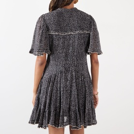 Model wearing Isabel Marant Etoile dress in black and ecru spot print, flutter sleeves, tiered skirt, back view showing yoke seam detail