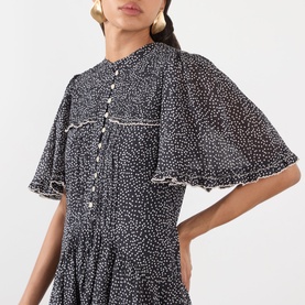 Model wearing Isabel Marant Etoile dress in black and ecru spot print, with flutter sleeves, button front, and frill trim detailing