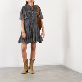 Model wearing Isabel Marant Etoile black and ecru cotton mini dress with flutter sleeves and button front, styled with tan cowboy boots and brown bag.