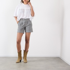 Model wearing Isabel Marant Etoile Douna Embroidered Blouse in white with grey tailored shorts and tan cowboy boots