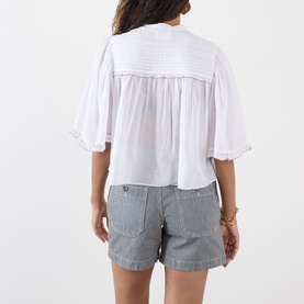 Model wearing Isabel Marant Etoile Douna Embroidered Blouse in white, back view, with ruffled cuffs, styled with grey striped shorts.