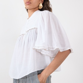 Model wearing Isabel Marant Etoile Douna Embroidered Blouse in white, with ruffled cuffs and scalloped trim, styled with striped trousers