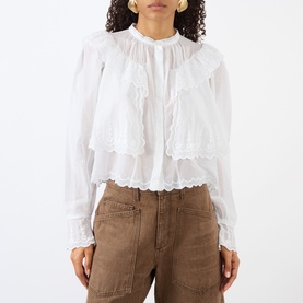 Model wearing Isabel Marant Etoile white cotton blouse with ruffle tiers and broderie trim, styled with tan trousers.
