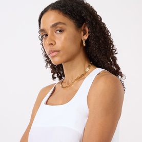 Model with Jenny Bird Nelle Slim Hoop Earrings in gold-toned 14K plated steel, polished finish. Styled with gold chain necklace and white vest.