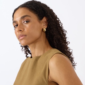Model with Jenny Bird Nelle Hoop Earrings in gold-tone, polished finish with cylindrical backing, styled with a khaki sleeveless top