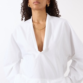 Model with Jenny Bird Dhani Chain Necklace in gold, polished chunky links, styled with a white deep V-neck top.