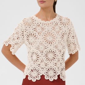 Model wearing Kaffe broken white floral crochet lace short-sleeve top with scalloped hem, styled with red trousers
