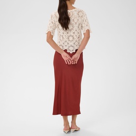Model wearing Kaffe broken white crochet floral top with flutter sleeves, styled with rust-red midi skirt and silver mule heels