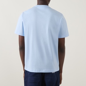 Model wearing Lacoste Croc Logo T-Shirt in Rill blue, rear view showing crew neck, short sleeves and straight hemline. Styled with navy trousers.