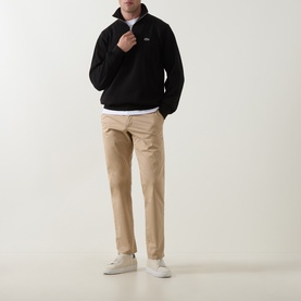 Model wearing Lacoste black cotton half-zip sweatshirt, styled with beige chinos and white trainers.