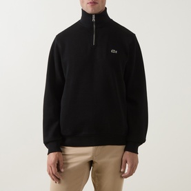 Model wearing Lacoste black cotton half-zip sweatshirt with ribbed high neck, small crocodile logo, styled with beige trousers.