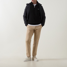 Model wearing Lacoste black cotton half-zip sweat with beige chinos, white t-shirt layered underneath, and white trainers.