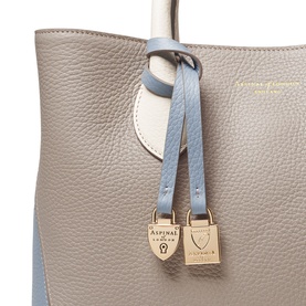 Aspinal of London Sky Blue tote bag close-up showing pebbled leather, colour-block panels, and gold padlock charm detail.