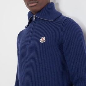 Model wearing Moncler navy wool half-zip knit jumper with ribbed texture and branded patch logo at chest.