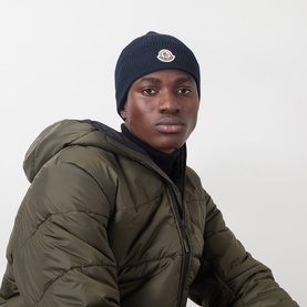 Model with Moncler Ribbed Logo Beanie Hat in navy, ribbed knit with logo patch. Styled with olive puffer jacket.