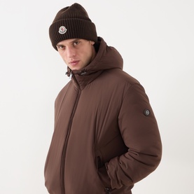 Model with Moncler Logo Badge Ribbed Beanie Hat in brown, half-brioche ribbed knit with logo badge, styled with matching brown hooded puffer jacket