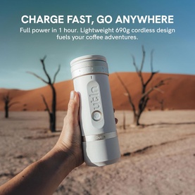 OutIn Fino Portable Electric Coffee Grinder in white, handheld against a desert landscape backdrop