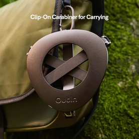OutIn Foldable Coffee Stand in black, shown with clip-on carabiner attachment for carrying, clipped to an olive green bag outdoors