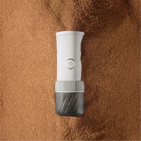OutIn Mino Portable Espresso Machine in grey, compact handheld design with white body and dark grey base, shown on coffee grounds background
