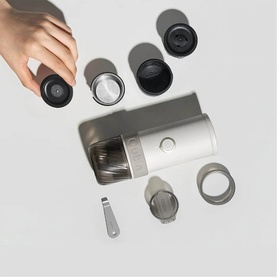 OutIn Mino Portable Espresso Machine in grey, shown disassembled with components including lid, filter, and carry tool laid flat