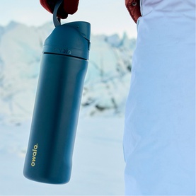 Owala FreeSip 24oz Water Bottle in Winter Nights teal, held by model outdoors in snowy setting, with carry loop visible at top