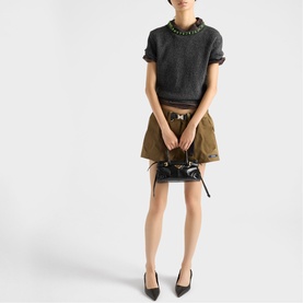 Model carrying Prada Accessories black small bag with gold-tone hardware, styled with dark knit top and khaki mini skirt
