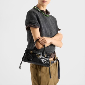 Model carrying Prada Accessories black leather bag with gold hardware and tassel detail, styled with grey top and khaki trousers.