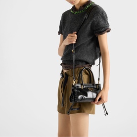 Model carrying Prada Accessories black mini bag with gold hardware and crossbody strap, styled with grey knit top and khaki shorts