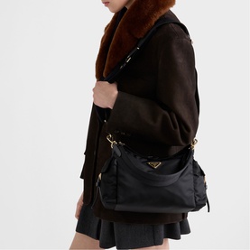 Model carrying Prada black nylon shoulder bag with gold-tone hardware and multi-pocket design, styled with dark mini skirt and brown faux fur collar