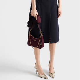 Model carrying Prada Accessories burgundy shoulder bag with gold-tone chain strap and triangle logo, styled with navy dress and nude heels