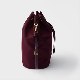 Burgundy canvas drawstring bucket bag with gold-tone hardware, adjustable leather strap and buckle detail, side view