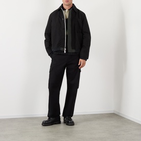 Model wearing SACAI Reversible Bomber Jacket in black with point collar, zip fastening, styled with black trousers and chunky leather shoes.